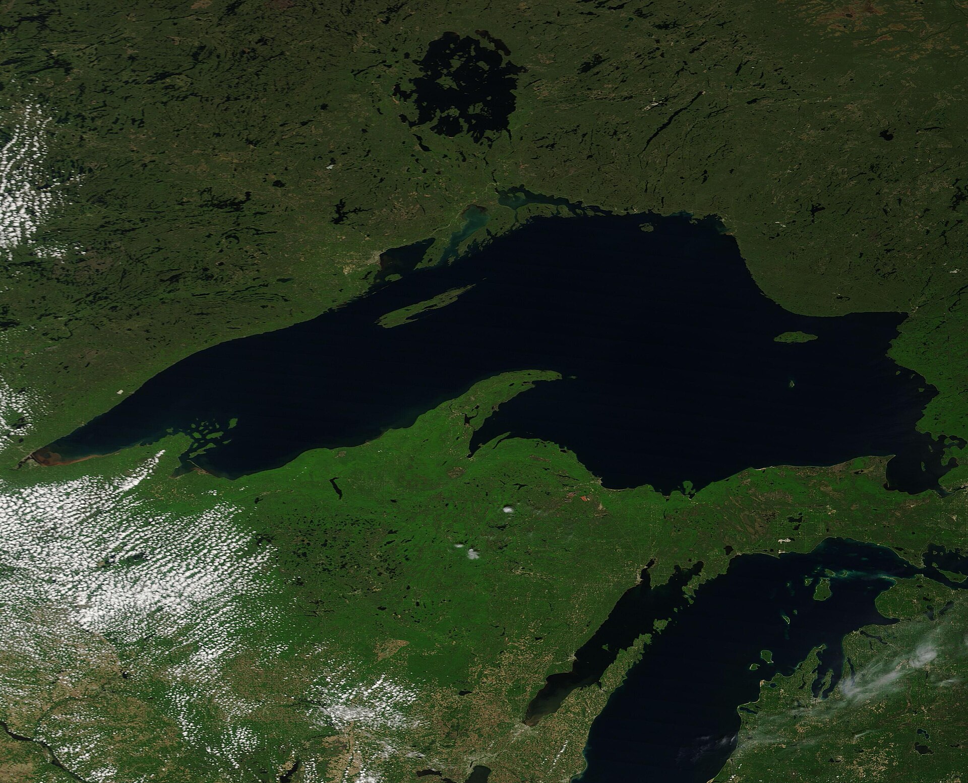 Satellite view of Lake Superior, the dark lake surrounded by green
                forested land, with the Ontario shoreline along its northern edge.